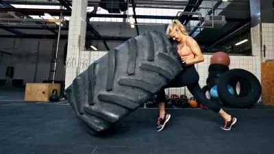 A determined woman lifts a large tire in a bright, industrial gym, showcasing strength and focus.
