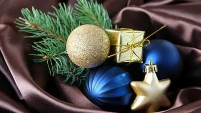 A festive arrangement of gold and blue ornaments, gifts, and pine on rich brown satin.